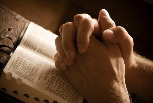 Hands folded in prayer on an open Bible